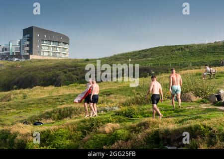 Eine Gruppe junger männlicher Urlauber trocknet nach dem Schwimmen im Meer in Towan Head in Newquay in Cornwall aus. Stockfoto