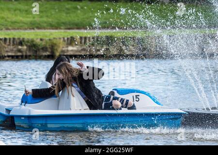 Ein aufgeregt Teenager Mädchen nimmt ein Selfie in einem Pedalo Als sie und ihre Freundin von der durchnässt wird Spray von einem dekorativen Brunnen auf Trenance Boating Stockfoto