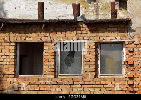 Altes, schäbiges Haus mit einer Backsteinfassade und einem kaputten Glasfenster Stockfoto
