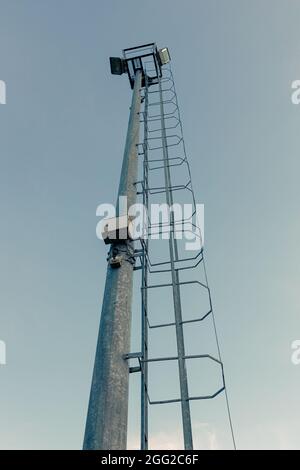 Hoher Mast von Spotlight mit Leiter am Abend blauen Himmel Hintergrund Stockfoto