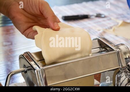 Pasta-Maschine, frische Pasta hausgemachte Zubereitung. Hand halten Teig Nahaufnahme Ansicht, Küchentisch Hintergrund Stockfoto