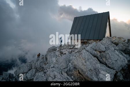 Ein Wanderer, der einen herrlichen Sonnenaufgang über einem Wolkenmeer in den Alpen auf dem Biwak genießt Luca Vuerich ist eine Berghütte für Bergsteiger und Wanderer, Stockfoto