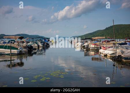 Cooperstown, NY, USA - 11. Aug 2021: Das blaue Wasser des Otsego Lake spiegelt an einem sonnigen Sommertag Cumuluswolken in der Nähe eines Docks mit Freizeitwasser wider Stockfoto
