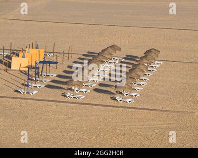 Sonnenliegen mit Strohschirmen am Strand Stockfoto