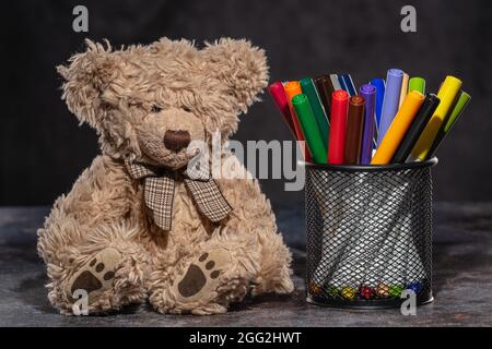 Zurück zur Schule. Bärenspielzeug neben bunten Markern, die auf dem Ständer stehen Stockfoto