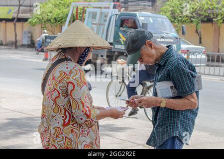 Ho Chi Minh, Vietnam - 30. Juni 2016: Szene eines alten Mannes, der auf der Straße von einer Frau in Ho Chi Minh City, Vietnam, Lottoscheine kauft Stockfoto