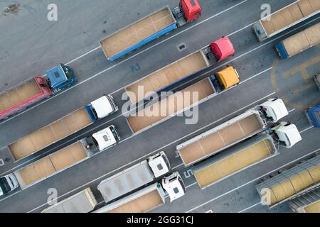 Frachttransport. Viele LKWs warten im Hafenhafen auf Entladung, Draufsicht von einem Quadcopter auf mit Getreide beladene LKWs. Concep Stockfoto