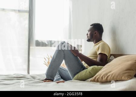 Seitenansicht eines afroamerikanischen Mannes, der eine Tasse Kaffee im Bett hält Stockfoto