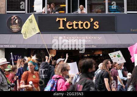 Von einem Fenster im Obergeschoss eines Steakhouse-Restaurants aus beobachten die Menschen, wie Mitglieder des Extinction Rebellion an einem protestmarsch vor dem Smithfield Market im Zentrum von London teilnehmen. Bilddatum: Samstag, 28. August 2021. Stockfoto