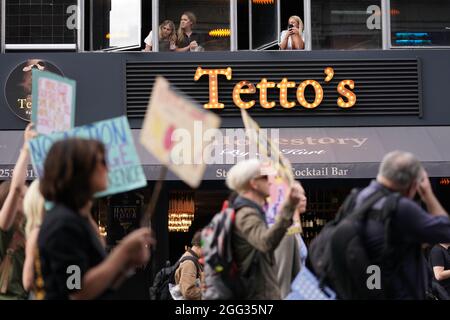 Von einem Fenster im Obergeschoss eines Steakhouse-Restaurants aus beobachten die Menschen, wie Mitglieder des Extinction Rebellion an einem protestmarsch vor dem Smithfield Market im Zentrum von London teilnehmen. Bilddatum: Samstag, 28. August 2021. Stockfoto