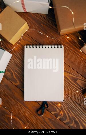Flaches Lay von leerem Notizbuch Girlande und Geschenkboxen auf Holztisch Hintergrund. Weihnachts- und Geburtstagskonzept. Platz für jedes Design kopieren. Raum für moderne kreative Arbeit des Designers. Stockfoto