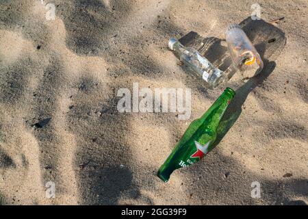 Hel, Polen - 08.02.2021: Detailaufnahme von leeren Bierflaschen und Gläsern, die am frühen Morgen nach einer Party am Vortag auf dem Strandsand liegen. Stockfoto