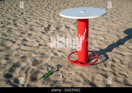 Hel, Polen - 08.02.2021: Leere Flaschen und Gläser liegen am Strand Sand unter Coca Cola Tisch am frühen Morgen nach der Party am Vortag. Stockfoto