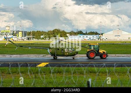 Riga, Lettland - 19. August 2021: Der Traktor zieht einen alten Militärhubschrauber (Ausstellung des Luftfahrtmuseums) durch das Flughafengebiet Stockfoto