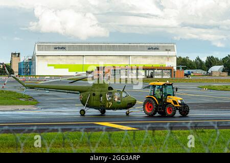 Riga, Lettland - 19. August 2021: Der Traktor zieht einen alten Militärhubschrauber (Ausstellung des Luftfahrtmuseums) durch das Flughafengebiet Stockfoto