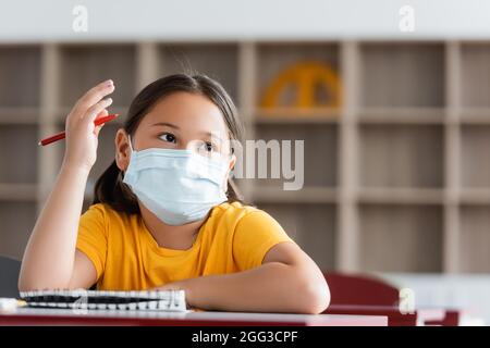 asiatische Mädchen in medizinische Maske heben Hand während der Lektion Stockfoto