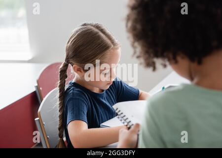 Verschwommener afroamerikanischer Junge, der in der Nähe des Schulmädchen im Klassenzimmer steht Stockfoto