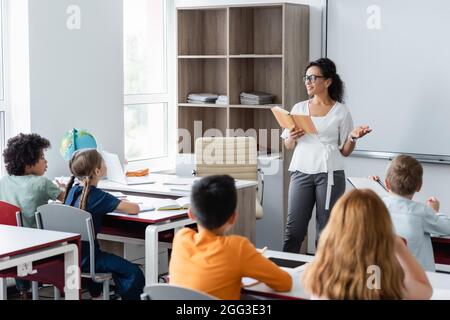 afroamerikanische Lehrerin zeigt mit der Hand beim Lesen des Buches im Klassenzimmer Stockfoto