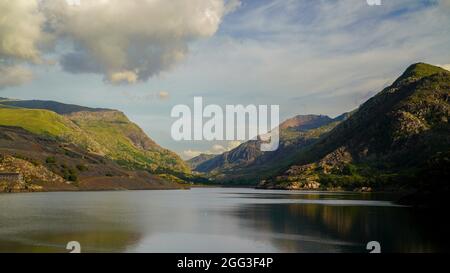 EIN BLICK ÜBER DEN LLYN PERIS STAUSEE BEI LLANBERIS, IM SCHATTEN DES SNOWDON BERGES, AN EINEM KLAREN UND SONNIGEN RUHIGEN NACHMITTAG Stockfoto