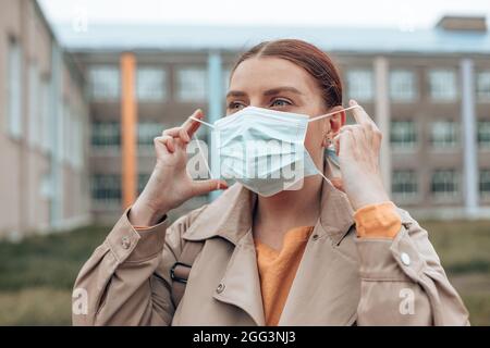 Glückliche Frau zieht ihre schützende medizinische Maske aus ihrem Gesicht, um nach dem Ende der Coronavirus-Pandemie frische Luft zu atmen. Wir haben gewonnen. Stockfoto