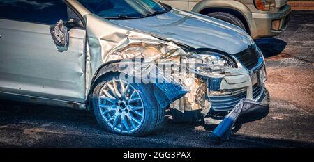 Silbernes Auto, das in einem weck mit abgerissenen Seiten, einem flachen Reifen und hängendem Heckfenster - Ansicht von rechts - war. Stockfoto