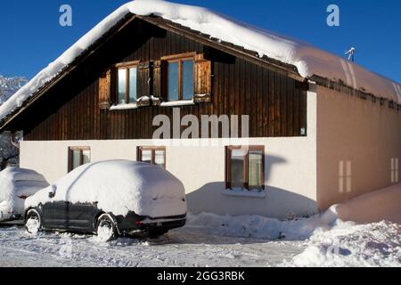 OBERSTAUFEN, DEUTSCHLAND - 29 DEZ, 2017: Typisches Holzhaus in den deutschen Alpen im Winter mit viel Schnee auf dem Dach und einem schneebedeckten Auto davor Stockfoto