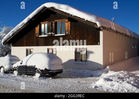 OBERSTAUFEN, DEUTSCHLAND - 29 DEZ, 2017: Typisches Holzhaus in den deutschen Alpen im Winter mit viel Schnee auf dem Dach und einem schneebedeckten Auto davor Stockfoto