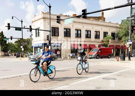 Zwei junge Männer, die mit dem Fahrrad unterwegs sind, überqueren die Blue Island Avenue in der Loomis Street im Stadtteil Pilsen in Chicago, Illinois, USA. Stockfoto