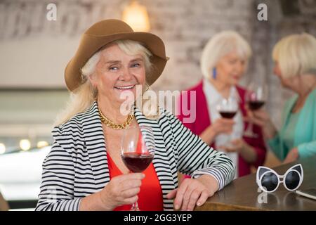 Fröhliche Frau in einem braunen Hut mit einem Glas Wein Stockfoto