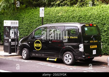 London, England - August 2021: London Taxi voll mit Strom betrieben, verbunden mit einer elektrischen Ladestation auf einer Stadtstraße. Stockfoto