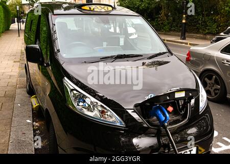 London, England - August 2021: London Taxi voll mit Strom betrieben, verbunden mit einer elektrischen Ladestation auf einer Stadtstraße. Stockfoto