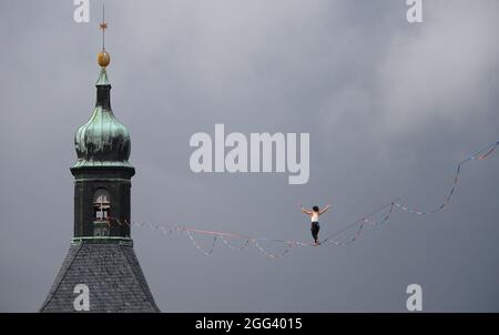 Hohnstein, Deutschland. August 2021. Beim Highline - und Family Festival balanciert ein Slackline-Läufer am Seil zwischen dem Schloss und der Stadtkirche der Sächsischen Schweiz. Die Slackline erstreckt sich über mehr als 100 Meter über den Marktplatz und ist 30 Meter lang. Rund um die Burg Hohnstein sind insgesamt 4 Seile installiert, die längste ist 360 Meter lang über das Polenztal. Quelle: Robert Michael/dpa-Zentralbild/dpa/Alamy Live News Stockfoto