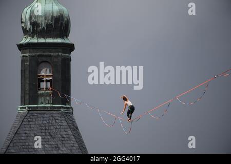 Hohnstein, Deutschland. August 2021. Beim Highline - und Family Festival balanciert ein Slackline-Läufer am Seil zwischen dem Schloss und der Stadtkirche der Sächsischen Schweiz. Die Slackline erstreckt sich über mehr als 100 Meter über den Marktplatz und ist 30 Meter lang. Rund um die Burg Hohnstein sind insgesamt 4 Seile installiert, die längste ist 360 Meter lang über das Polenztal. Quelle: Robert Michael/dpa-Zentralbild/dpa/Alamy Live News Stockfoto