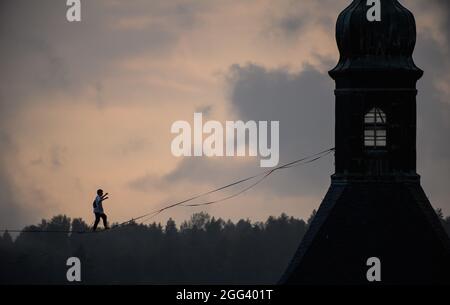 Hohnstein, Deutschland. August 2021. Ruben langer, Slackline-Weltrekordler, balanciert am Seil zwischen Schloss und Stadtkirche der Stadt in der Sächsischen Schweiz beim Highline - und Familienfest. Die Slackline erstreckt sich über mehr als 100 Meter über den Marktplatz und ist 30 Meter lang. Rund um die Burg Hohnstein sind insgesamt 4 Seile installiert, die längste ist 360 Meter lang über das Polenztal. Quelle: Robert Michael/dpa-Zentralbild/dpa/Alamy Live News Stockfoto