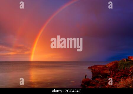 Mann Angeln mit einem schönen Regenbogen in der Ferne, Cresswell, Druridge Bay, Northumberland, England, VEREINIGTES KÖNIGREICH. Stockfoto