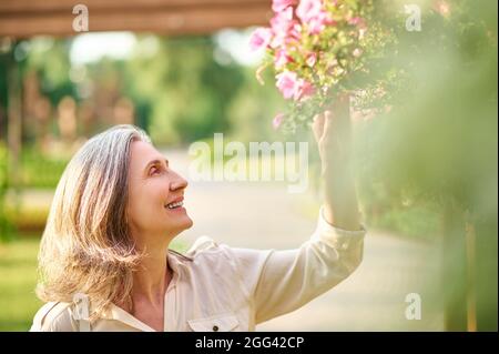 Glückliche Frau berührt Blumen im Park Stockfoto