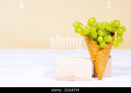 Grüne Traube in süßem Waffelkegel auf Holzständern auf hellorangefarbenem Hintergrund. Gesunde Ernährung, saisonale Ernte der Früchte. Raum kopieren, Gleichgewicht Stockfoto