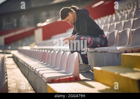 Sportmädchen entspannt sich auf den Stufen vor dem Training mit Musik und bereitet sich auf den Start des Rennens vor. Sportkonzept. Stockfoto