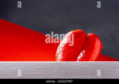 Foto eines nassen roten Pfeffers auf einer weißen Planke mit rotem Hintergrund und aufgenommen aus der untersten Perspektive.das Foto wurde im horizontalen Format aufgenommen. Stockfoto