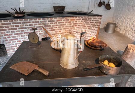 Dinant, Wallonien, Belgien - 8. August 2021: Festung Zitadelle. Schwarzer Holztisch mit Geschirr und Essen in der Küche mit Kamin im Rücken. Stockfoto