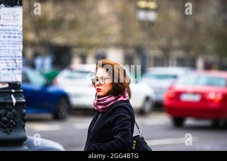 Porträt einer Frau mit schwarzem Wintermantel und buntem Schal, die auf ein Taxi wartet. Bukarest, Rumänien, 2019. Stockfoto