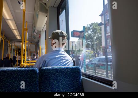 Innenansicht und ausgewählte Fokusansicht auf der Rückseite eines männlichen Passagiers mit Gesichtsschutzmaske, der in der Stadtbahn oder im Zug in Deutschland sitzt. Stockfoto