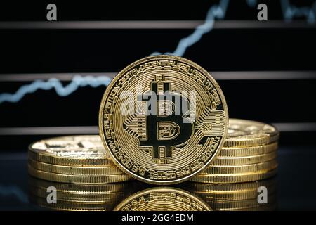 Bitcoin physische Münze aus der Nähe, vor einem Kursdiagramm Stockfoto