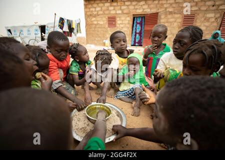 Eine Gruppe von Kindern essen rund um ein gemeinsames Gericht aus Hirsepaste und Baobab-Blatt-Eintopf, wahrscheinlich ihre einzige Mahlzeit des Tages. Diese Großfamilie wurde aufgrund von Gewalt und Unsicherheit vertrieben und steht nun vor Hunger und Nahrungsmittelknappheit. Provinz Kossi, Burkina Faso, Westafrika. Stockfoto