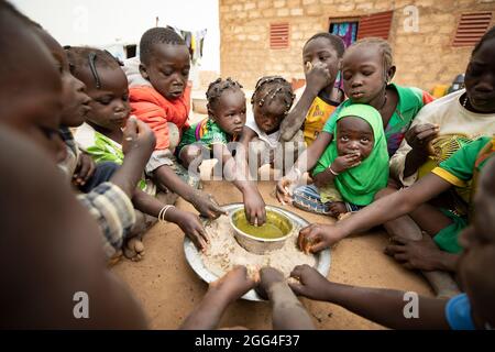 Eine Gruppe von Kindern essen rund um ein gemeinsames Gericht aus Hirsepaste und Baobab-Blatt-Eintopf, wahrscheinlich ihre einzige Mahlzeit des Tages. Diese Großfamilie wurde aufgrund von Gewalt und Unsicherheit vertrieben und steht nun vor Hunger und Nahrungsmittelknappheit. Provinz Kossi, Burkina Faso, Westafrika. Stockfoto