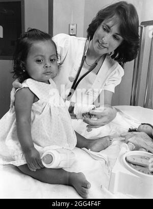 Austin Texas USA, um 1989: Krankenschwester im Kinderkrankenhaus umarmt junge Patientin auf einem Untersuchungstisch, um sie zu beruhigen. ©Bob Daemmrich Stockfoto