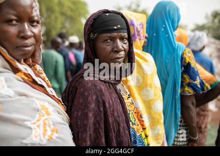 An einem Verteilungsort des IDP-Lagers in Nouna, Burkina Faso, Westafrika, stehen Frauen an, um Nahrungsmittelhilfe zu erhalten. Stockfoto