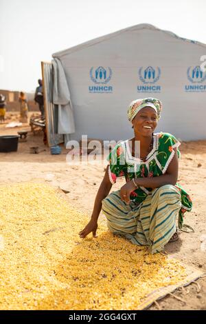 Traore Jeneba (20) wäscht und trocknet Mais vor ihrem Zelt in Nouna, Burkina Faso. Ihre Familie floh nach der Entführung ihres Schwiegervaters im Nordosten des Landes vor Gewalt und Unsicherheit und sieht sich hier nun vor Hunger und Not. Stockfoto