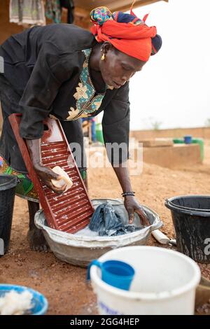 Eine Frau wäscht ihre Kleidung mit einem Waschbrett und Waschbecken außerhalb ihres Hauses in der Provinz Kossi, Burkina Faso, Westafrika. Stockfoto