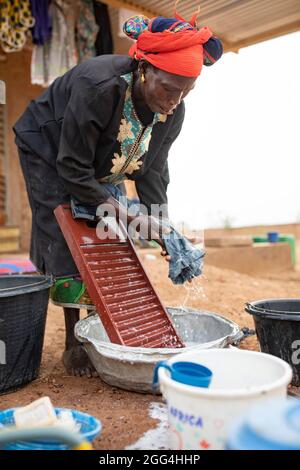 Eine Frau wäscht ihre Kleidung mit einem Waschbrett und Waschbecken außerhalb ihres Hauses in der Provinz Kossi, Burkina Faso, Westafrika. Stockfoto